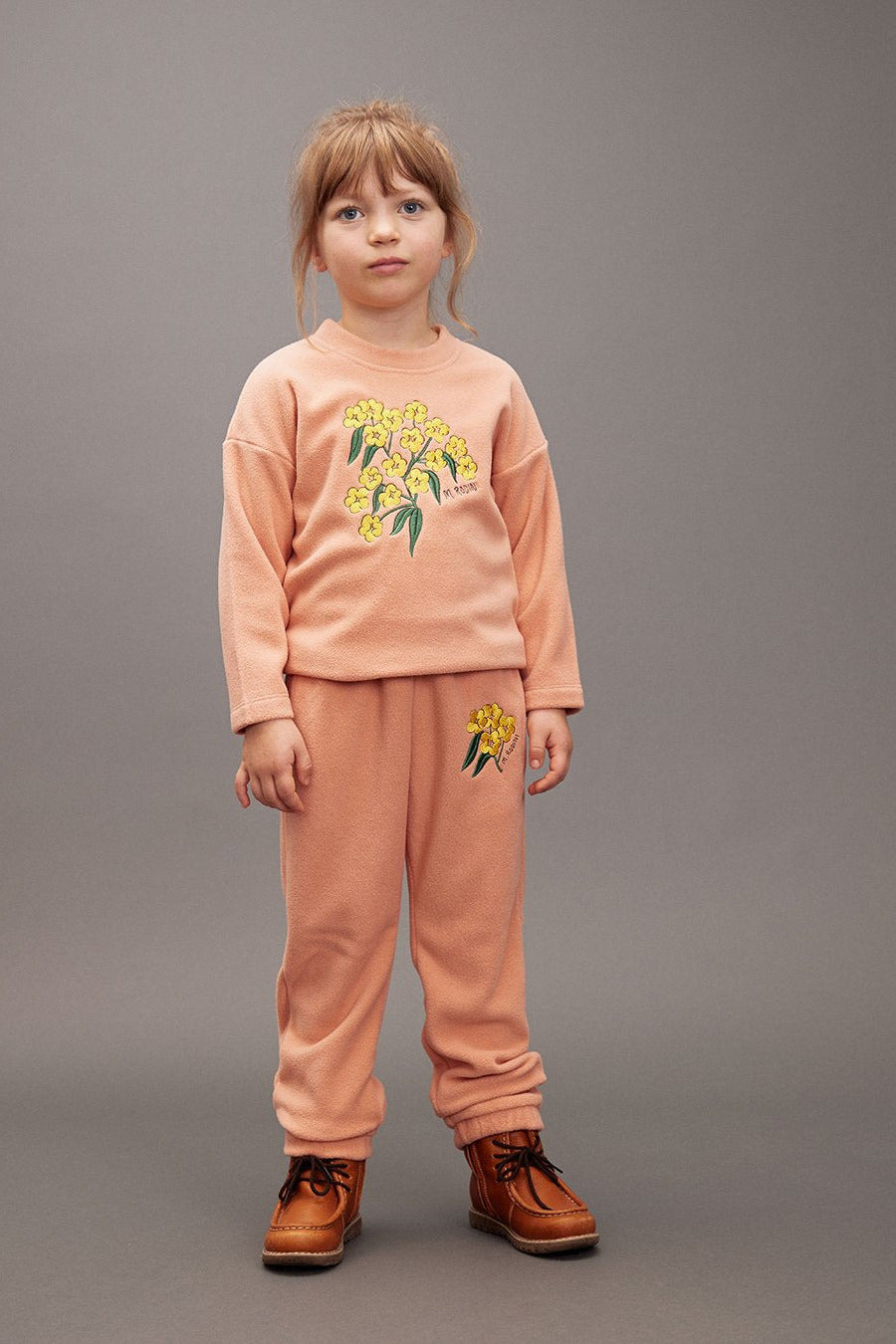 Child wearing a peach outfit with floral designs on a gray background - Little-ish