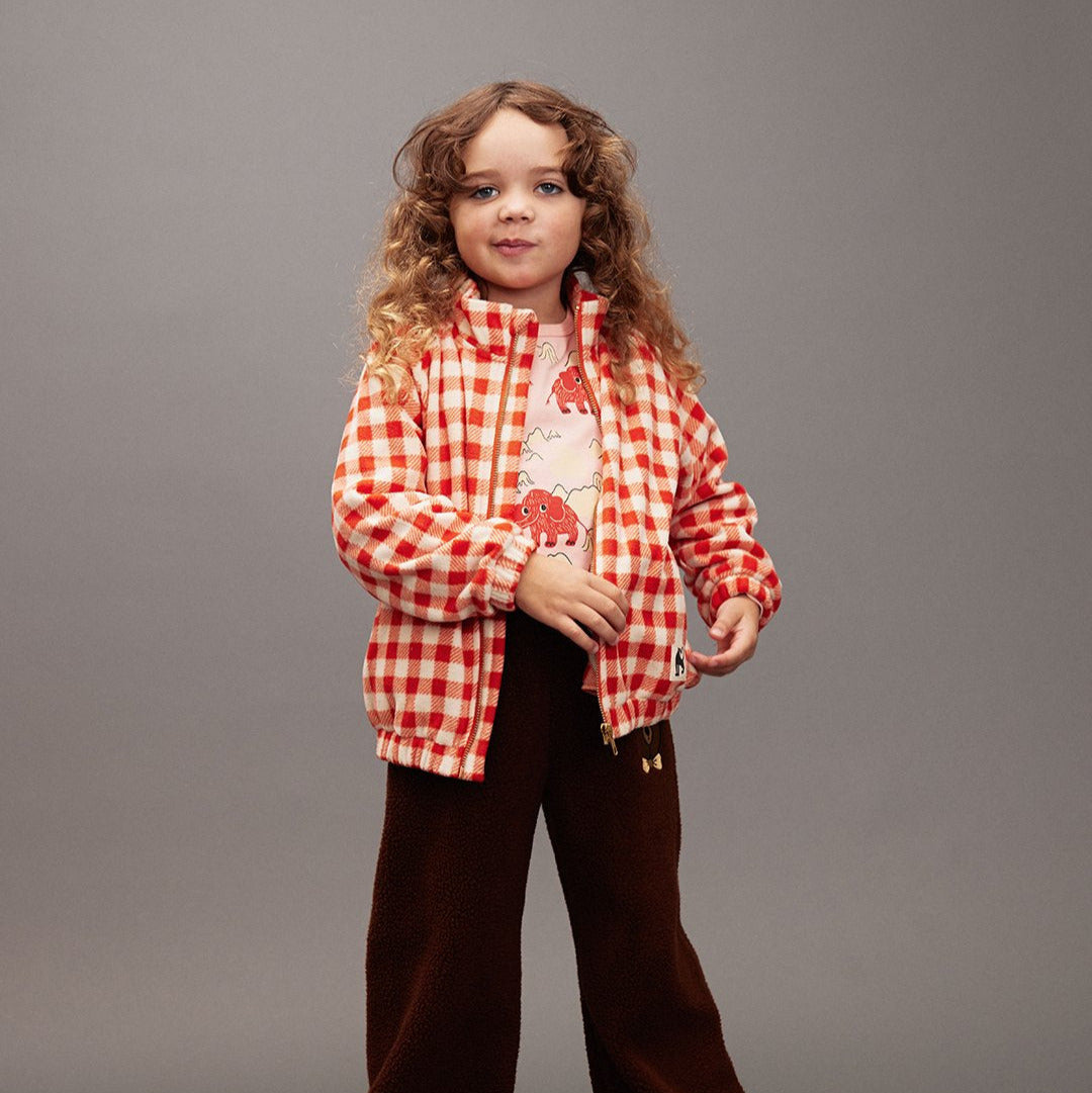 Child wearing a red checkered shirt and brown pants on a gray background
