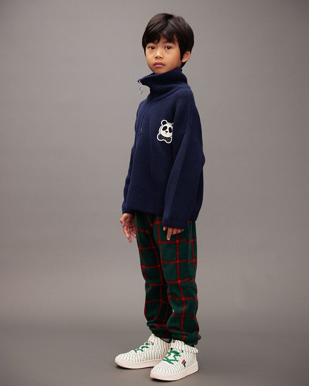 Child wearing a navy sweater with a panda design and plaid pants on a gray background