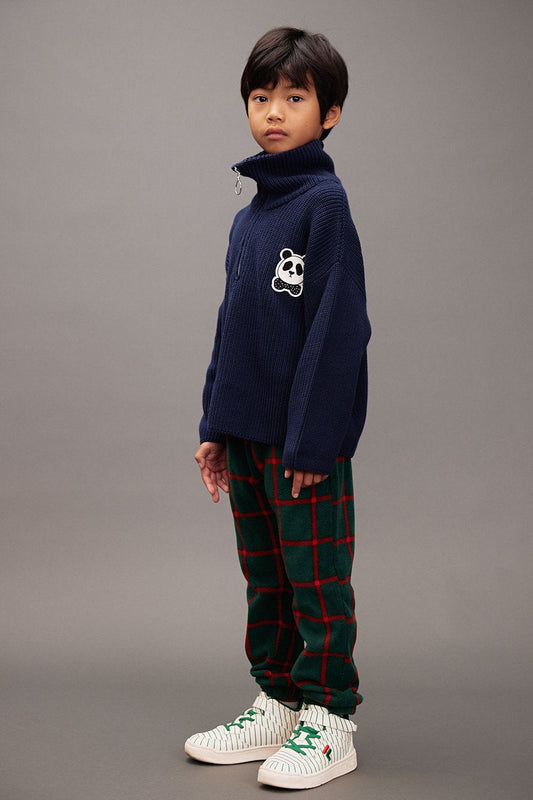 Child wearing a navy sweater with a panda design and plaid fleece pants on a green background