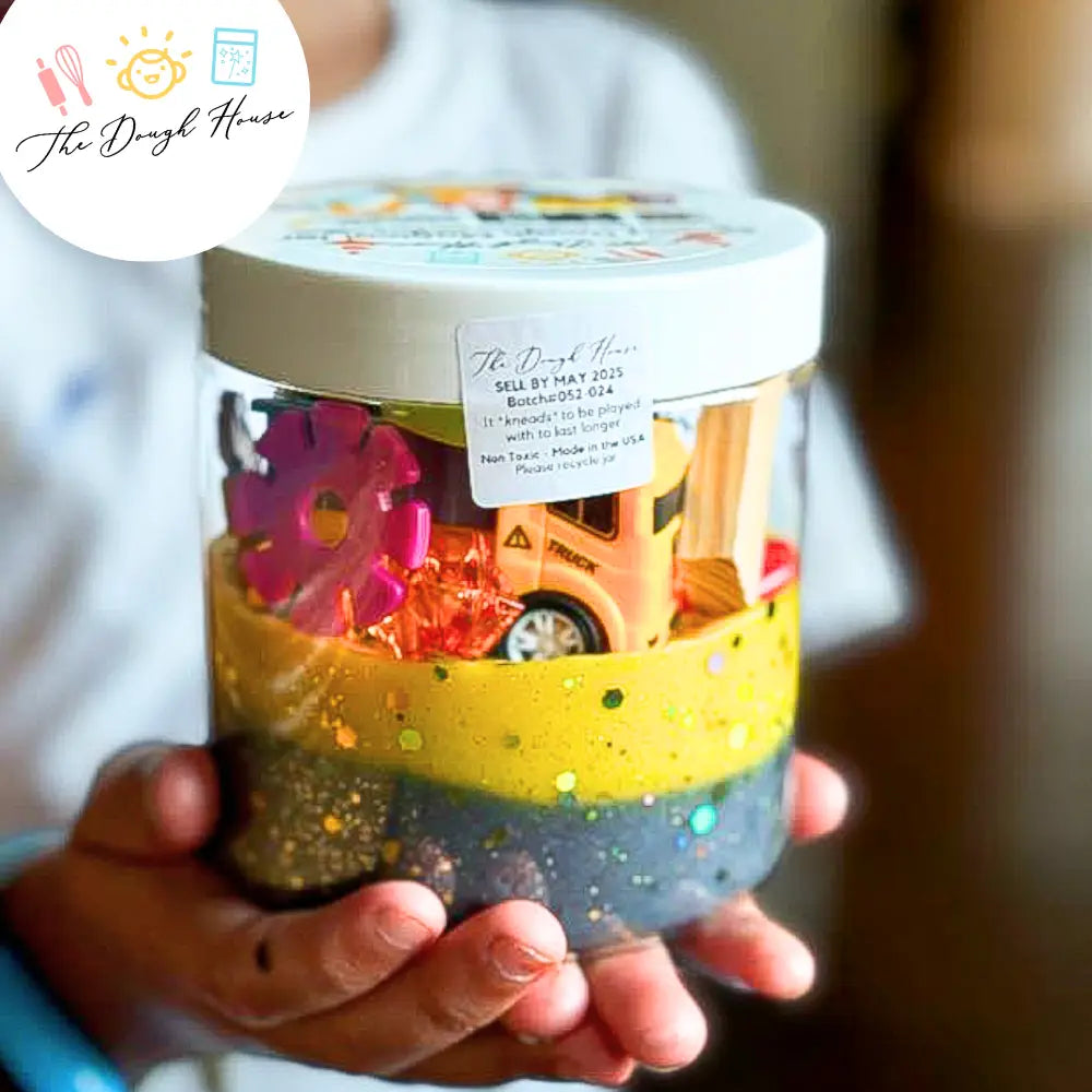Child's hand holding a jar filled with colorful toys, branded 'The Dough House'.