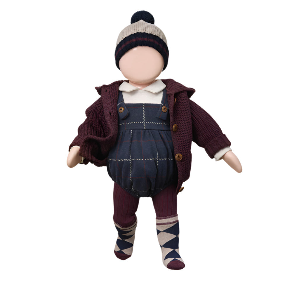 Doll wearing a maroon jacket, plaid overalls, and patterned socks on a white background