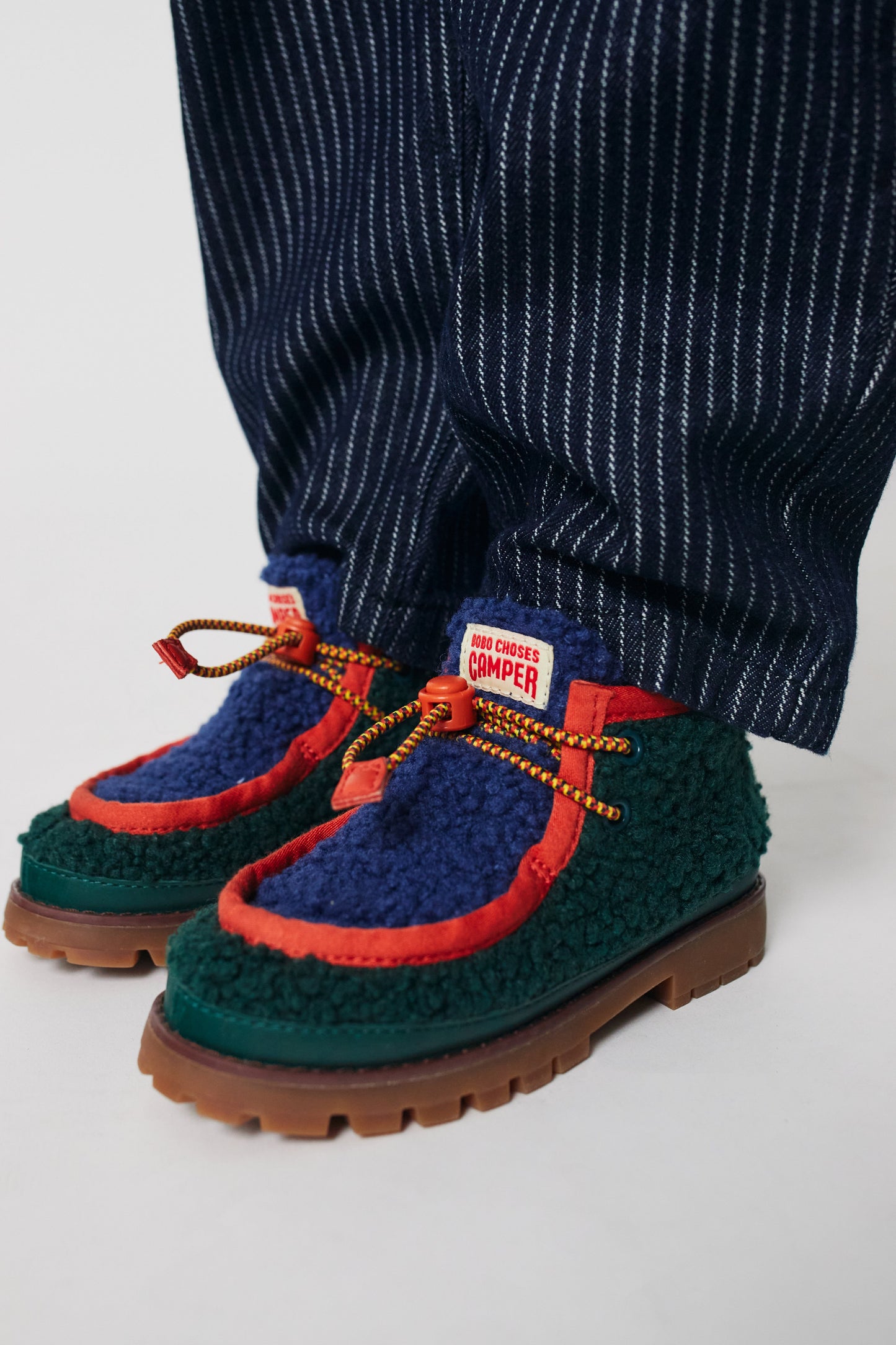 Green and blue shoes with red accents worn with navy pinstripe pants on a light gray background