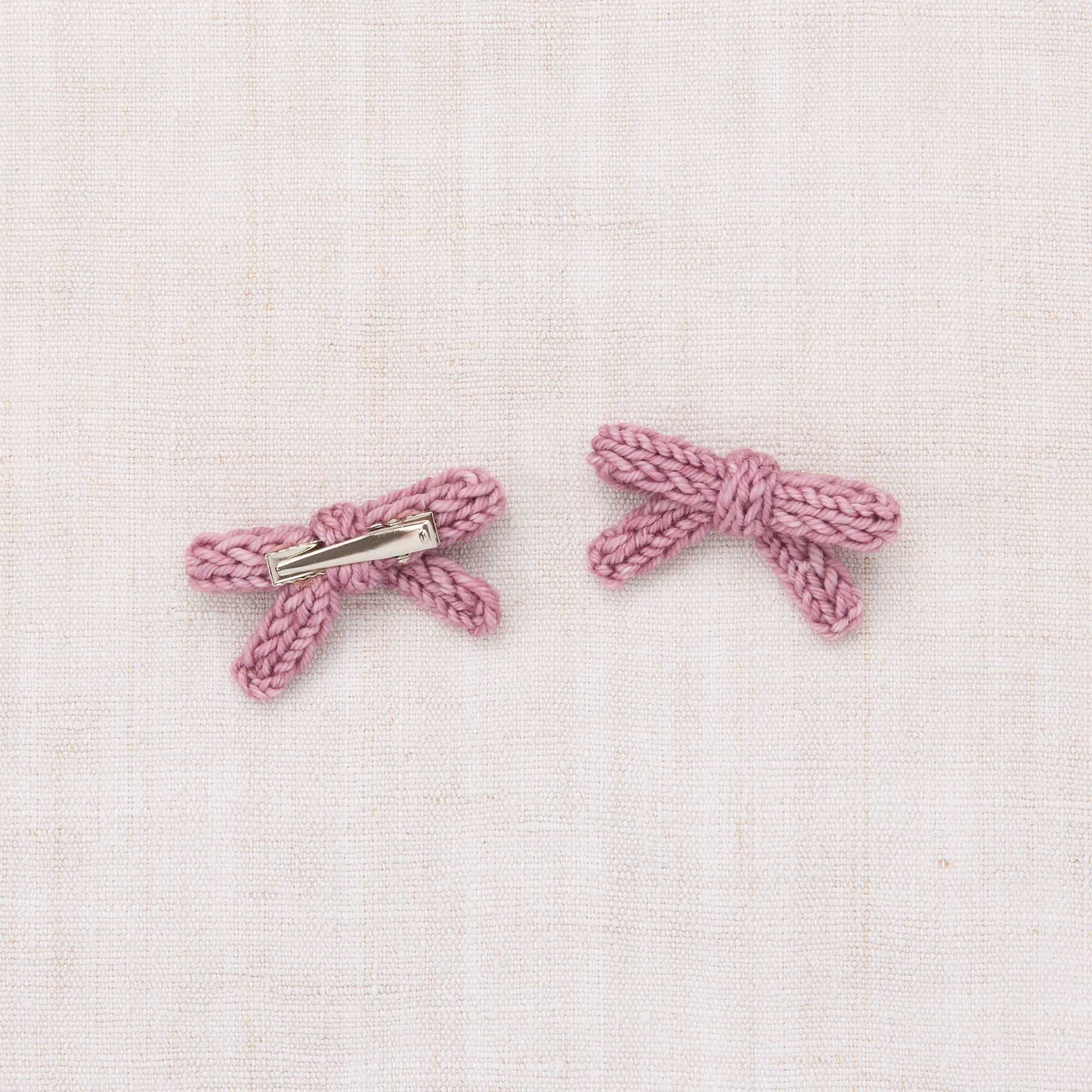 Pair of pink bow-shaped earrings on a light pink textured background - Little-ish