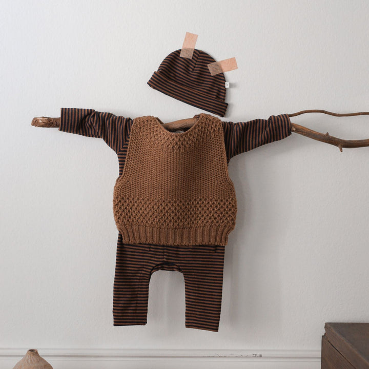 Brown knitted outfit with hat on a branch against a white wall.