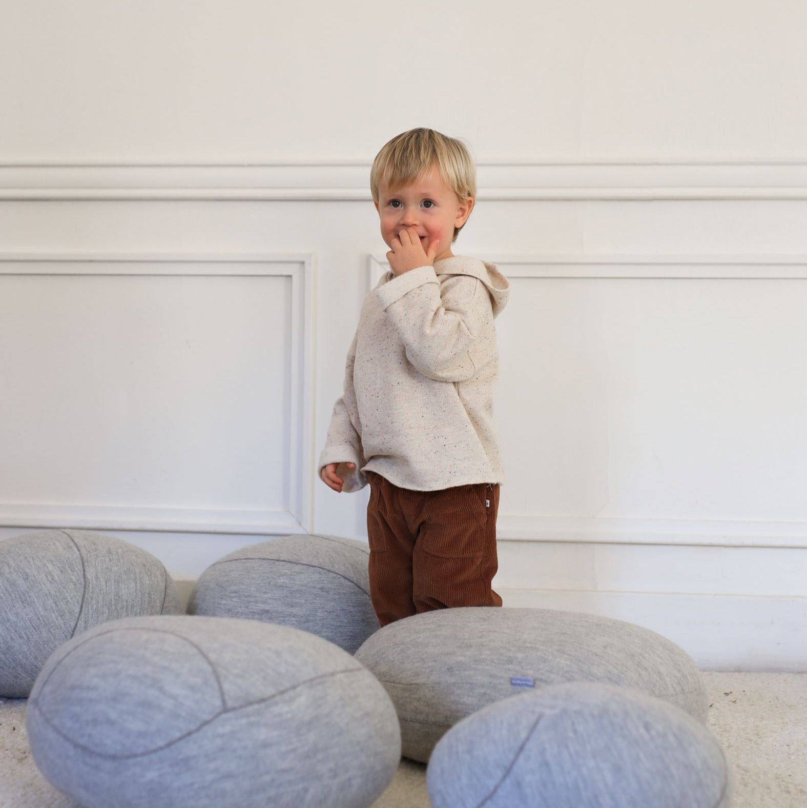 Child standing among gray bean bags against a white wall - Little-ish