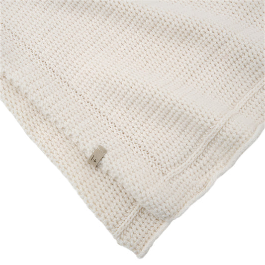 Close-up of a textured ecru wool knit blanket with a corner folded over on a white background