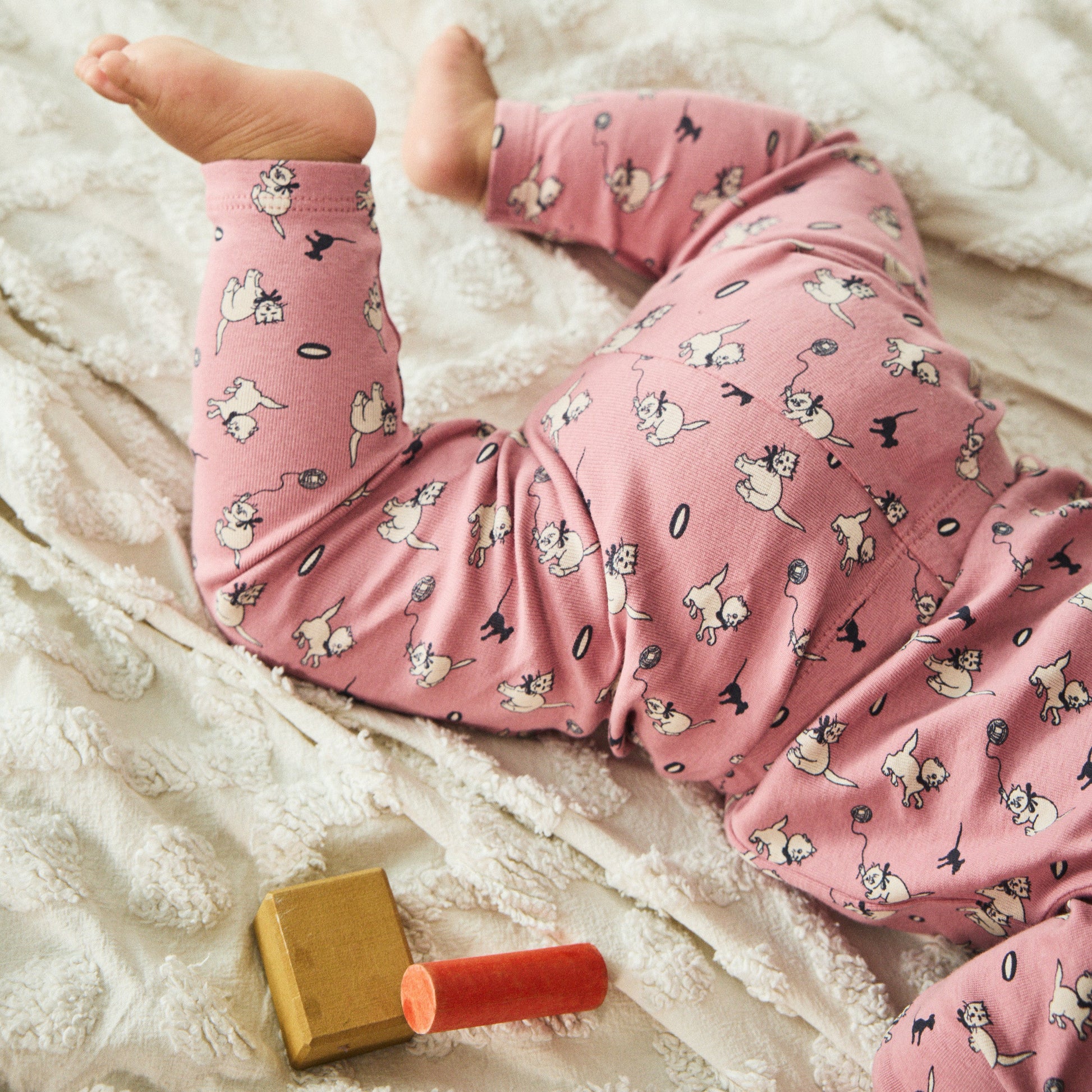 Baby in pink pants with a toy on a soft surface