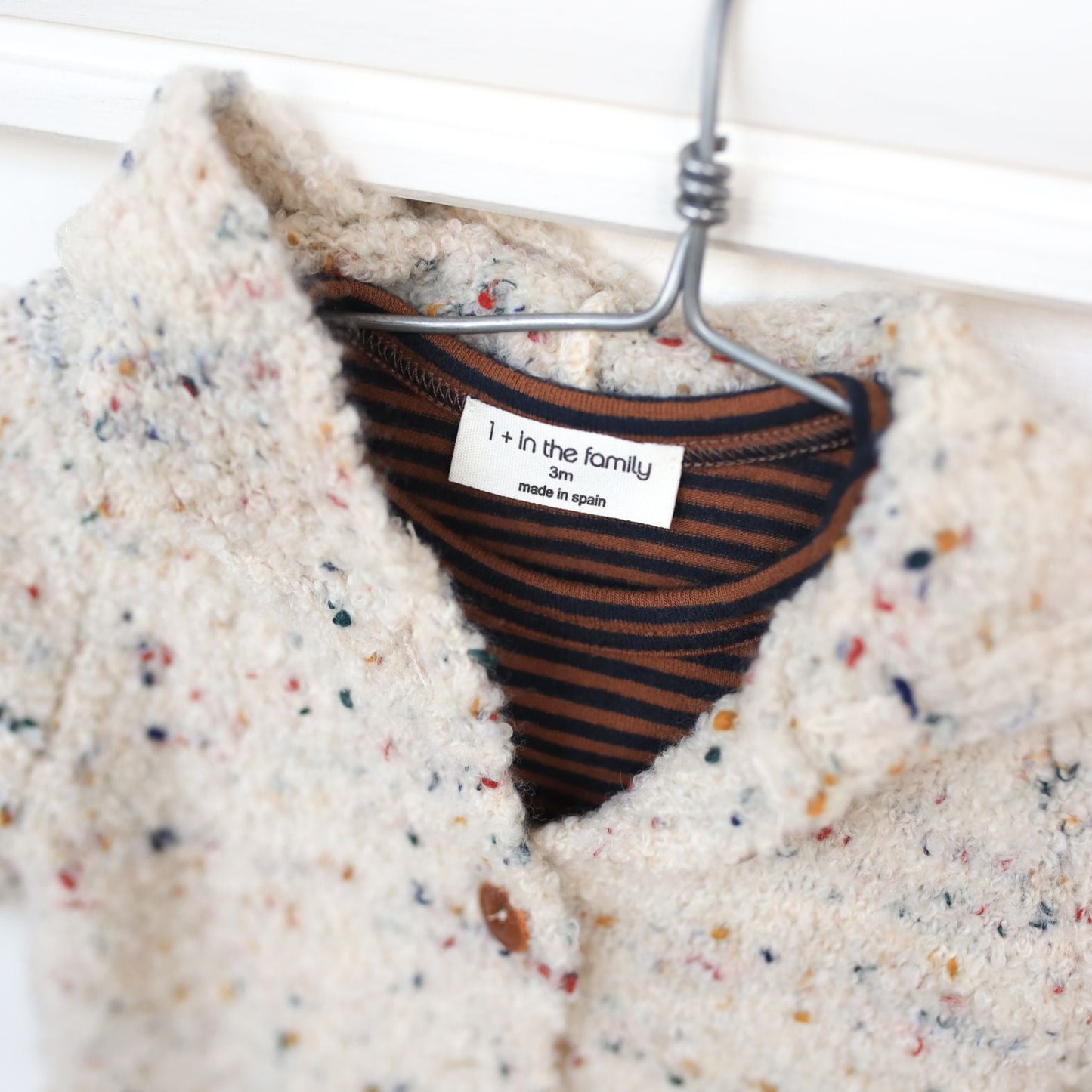 Textured sweater on a hanger with a striped shirt underneath