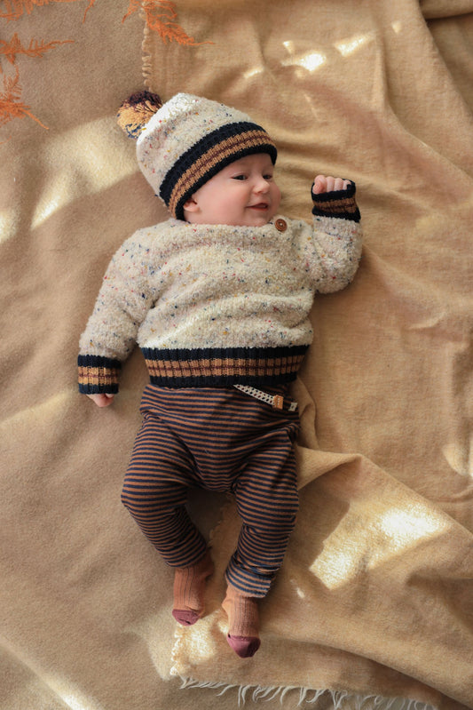 Baby wearing a striped sweater and hat lying on a beige blanket