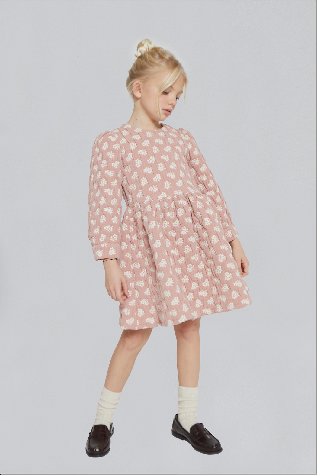 Young girl wearing a pink patterned dress on a light gray background