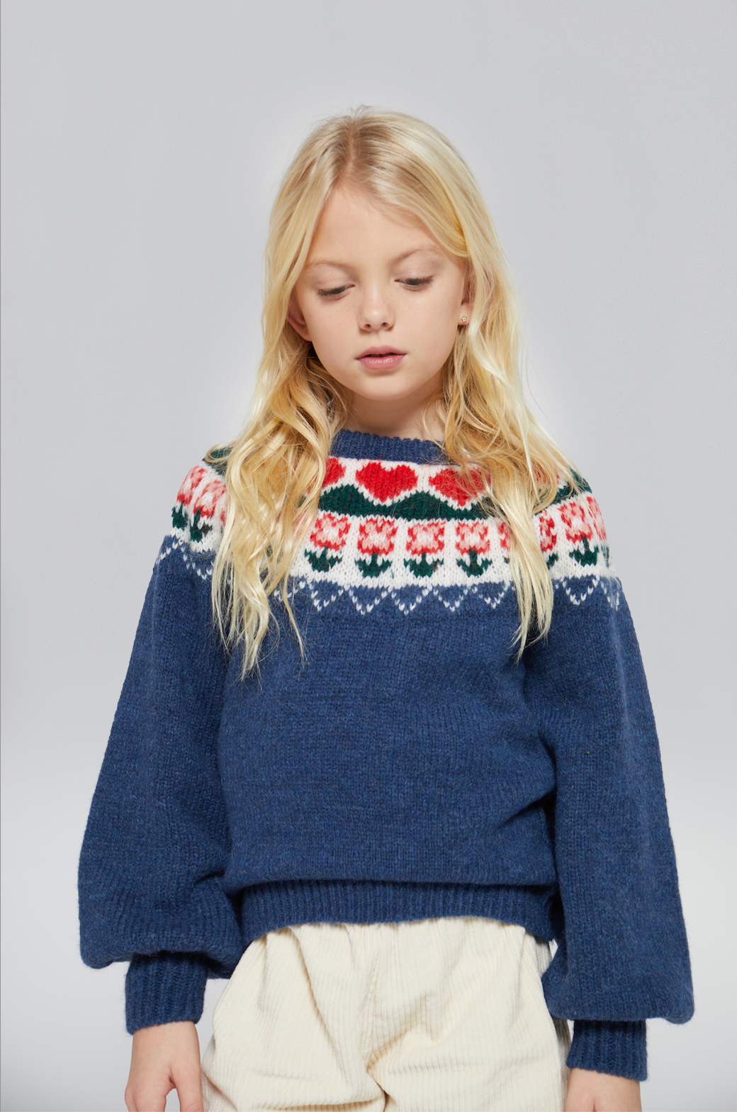 Young girl wearing a blue sweater with a colorful pattern on a plain background