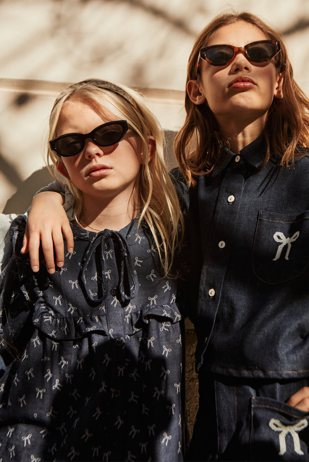 Two women wearing dark sunglasses and navy outfits with bow details outdoors.