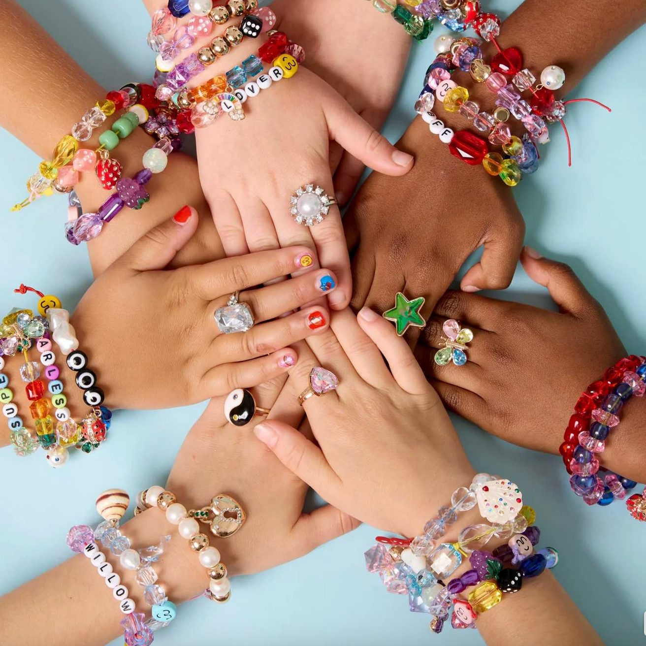 Children's hands with colorful bracelets and rings on a light blue background