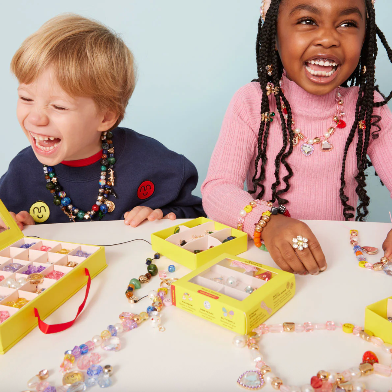 Two children making jewelry with colorful beads and tools on a table.