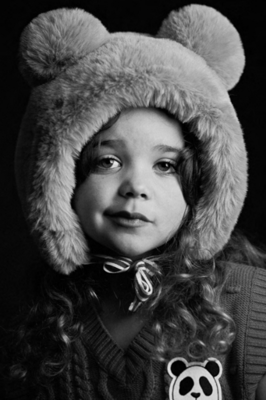 Black and white photo of a child wearing a fluffy hat with bear ears.