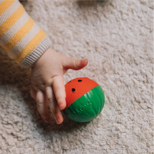 Child's hand holding a colorful ball with 'Bob & Co.' branding on a carpeted floor.