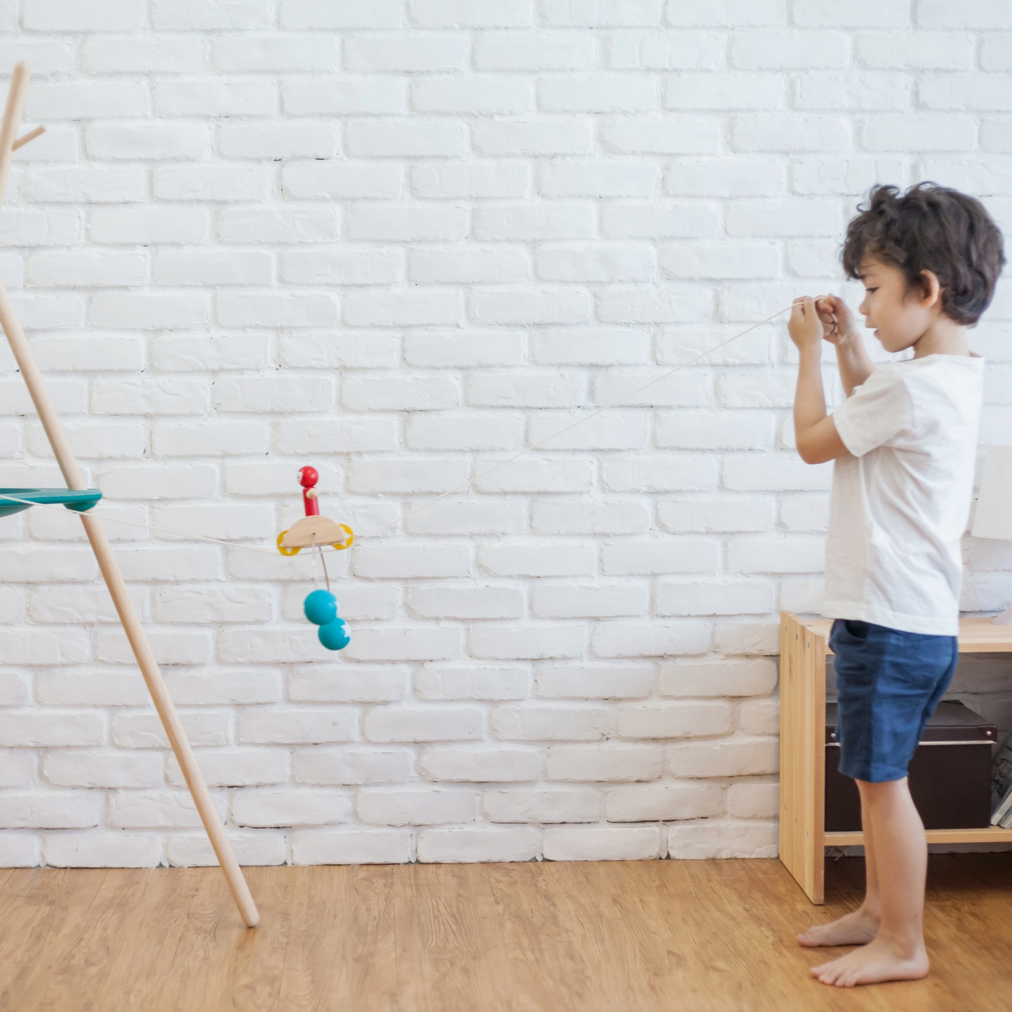 Child playing with toys in a room with a white brick wall and wooden floor. - Little-ish