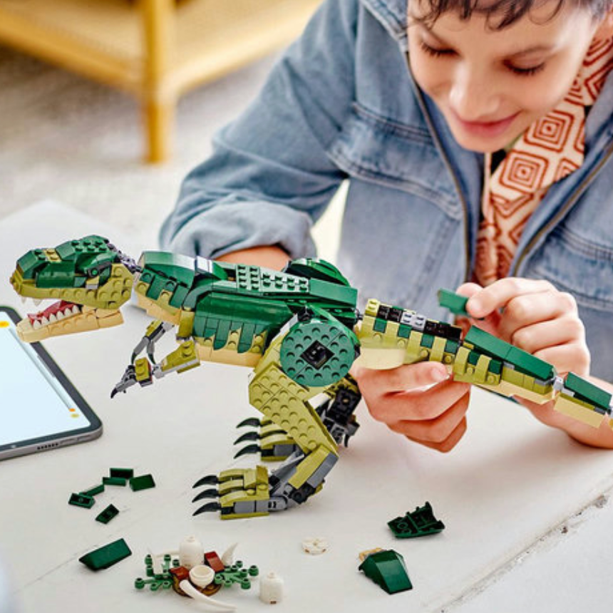 Child playing with a dinosaur toy set on a table, with a tablet in the background.