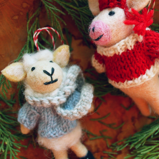 Two knitted animal toys, a sheep and a piglet, on a green leafy background.