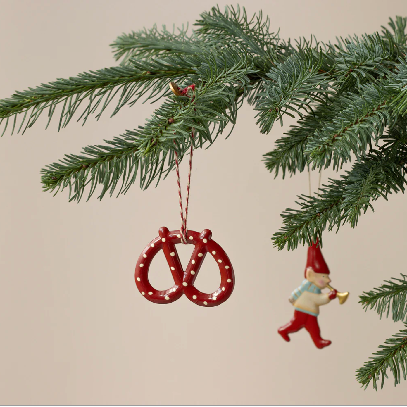 Decorative Christmas ornament with red pretzels and a gnome hanging from a tree branch.