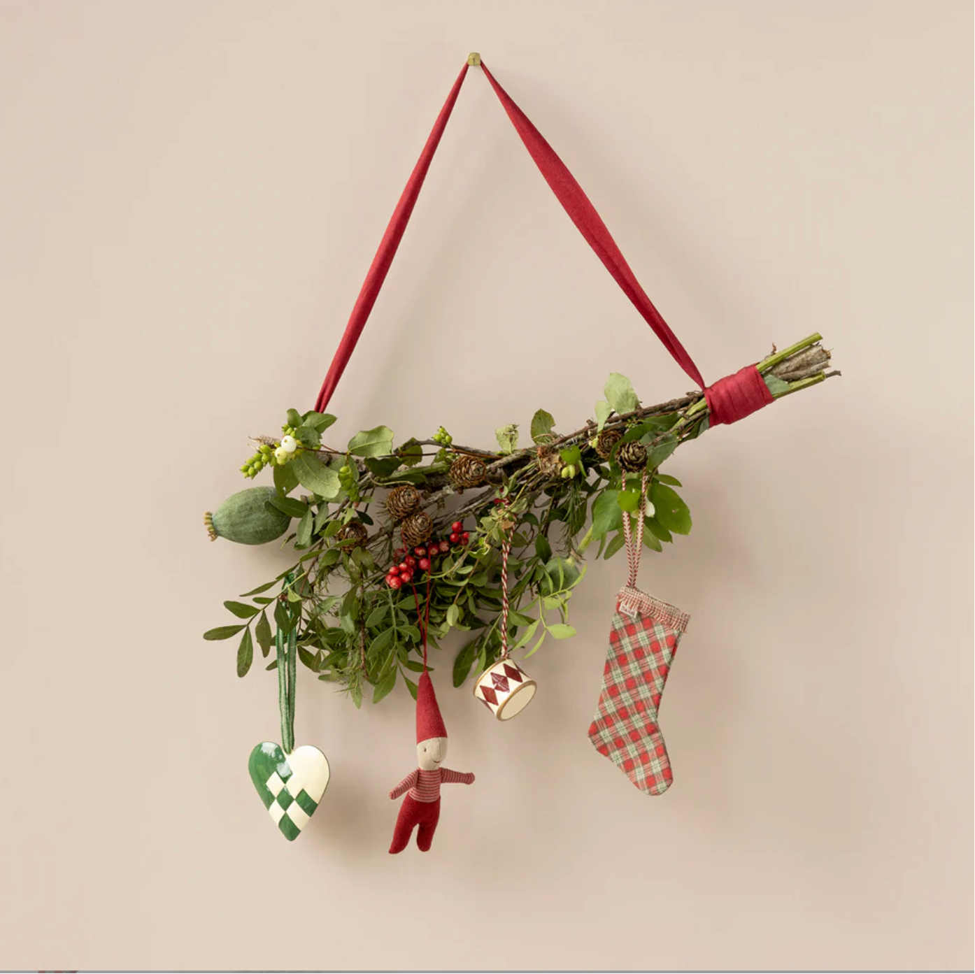 Decorative wall hanging with greenery, small figurines, and red ribbons on a beige background - Little-ish