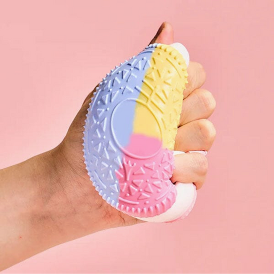 Hand holding a colorful textured object against a pink background