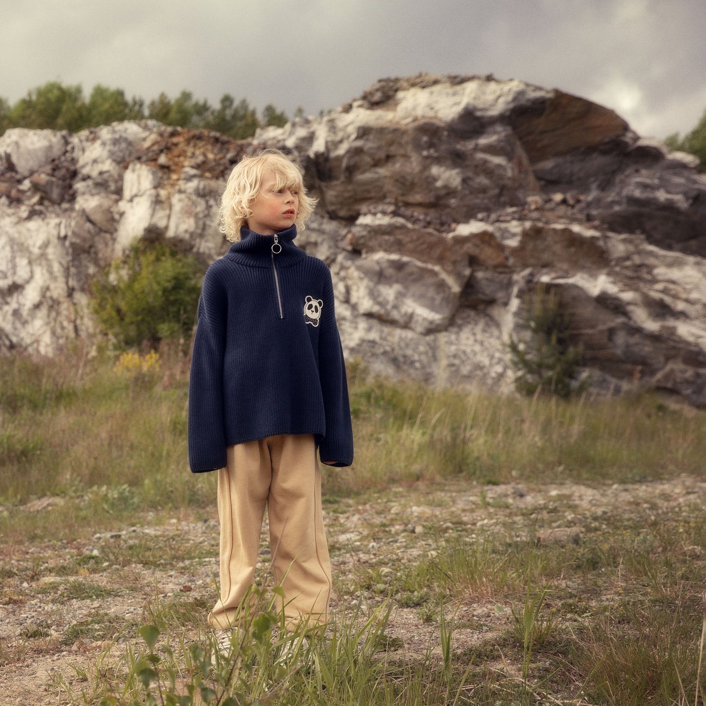 Person wearing a navy sweater with a white logo in a rocky landscape