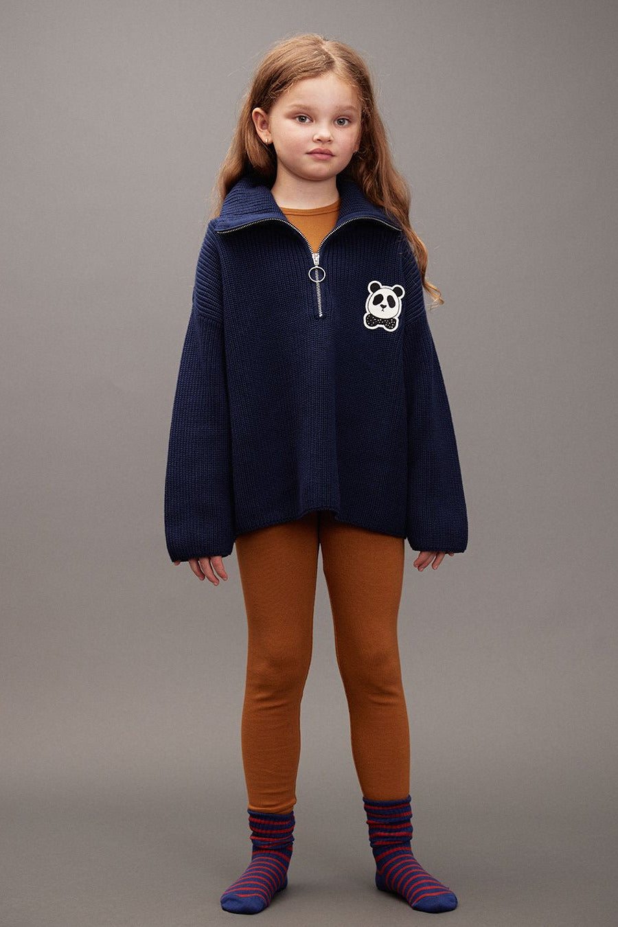 Young girl wearing a navy blue jacket with a panda design on a gray background