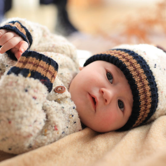 Baby wearing a knitted hat and coat lying on a soft surface