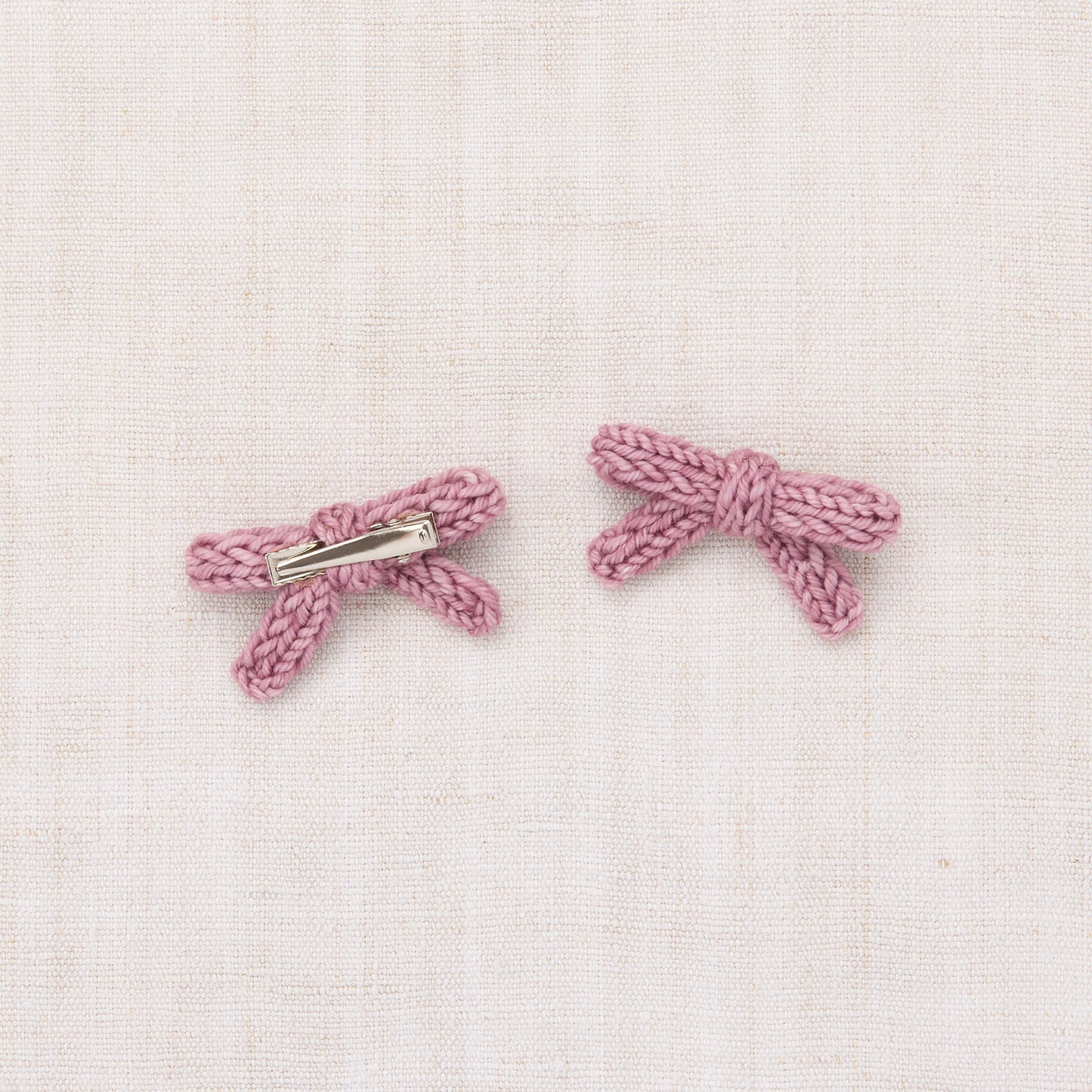 Pair of pink bow-shaped earrings on a light pink textured background