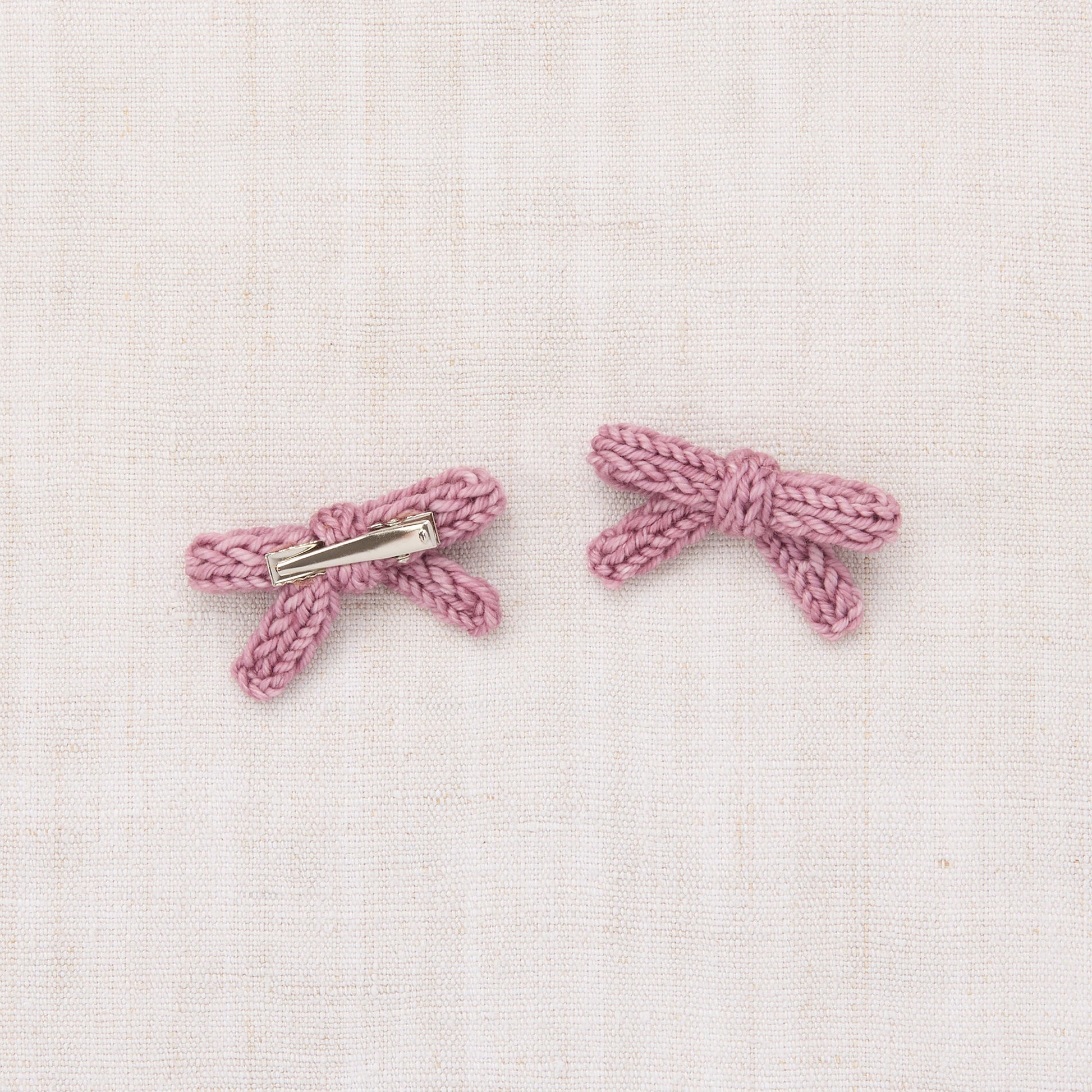 Pair of pink bow-shaped earrings on a light pink textured background