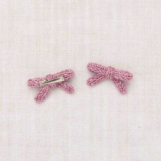 Pair of pink bow-shaped earrings on a light pink textured background