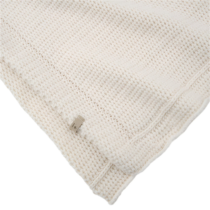 Close-up of a textured ecru wool knit blanket with a corner folded over on a white background