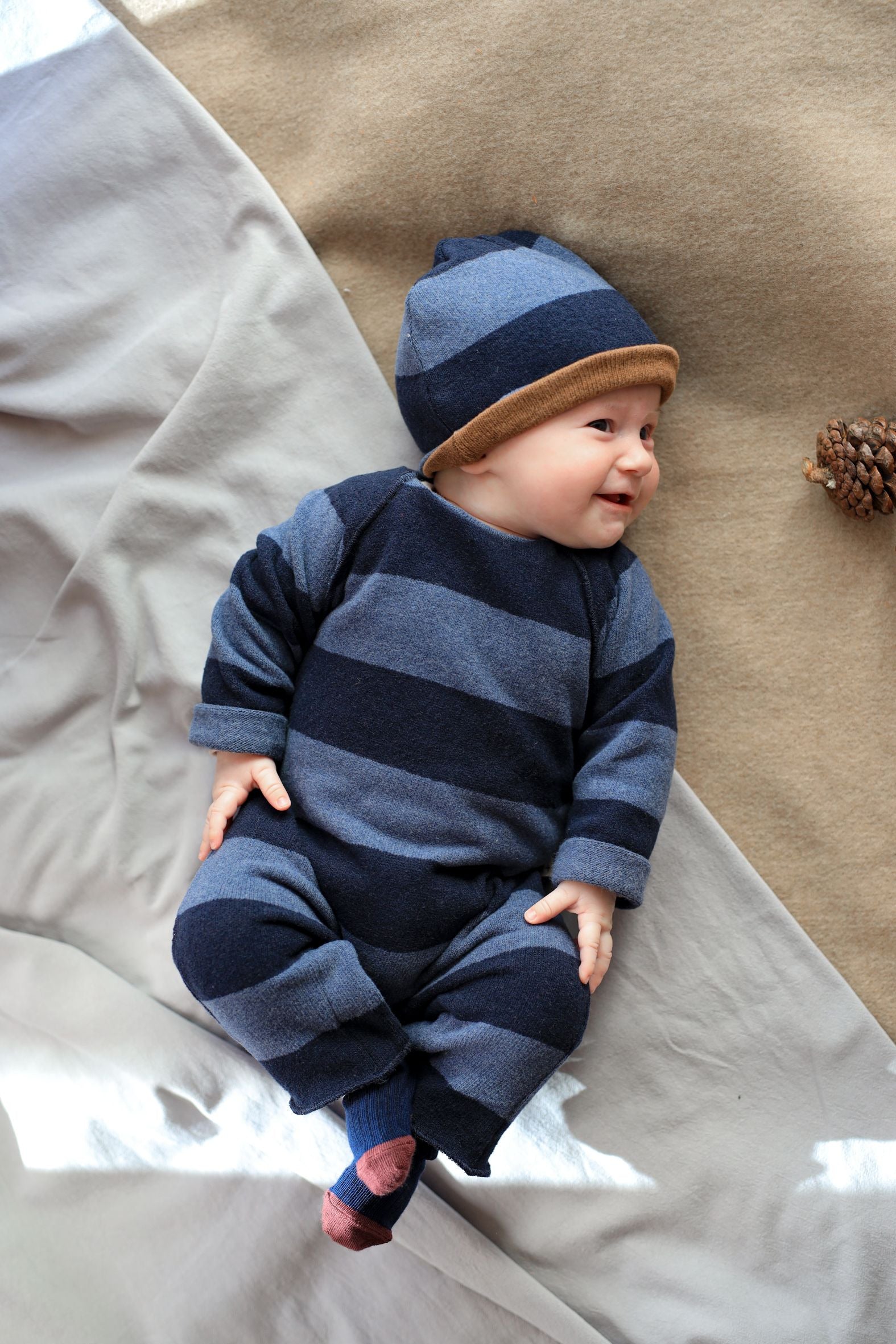 Baby wearing a blue striped outfit and hat lying on a textured surface - Little-ish