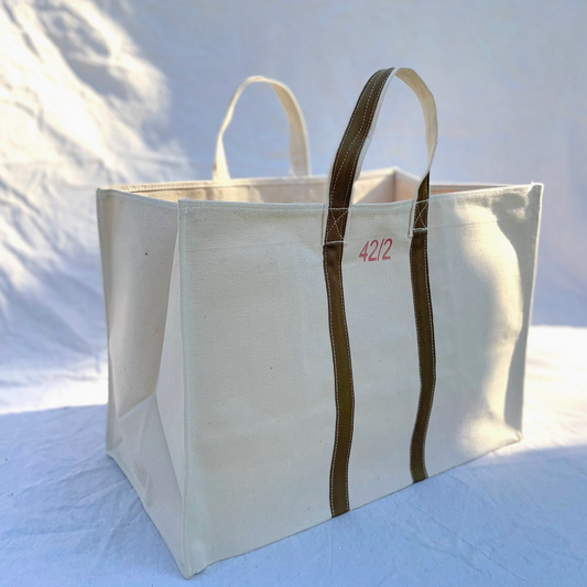 Large white tote bag with brown handles on a light blue background