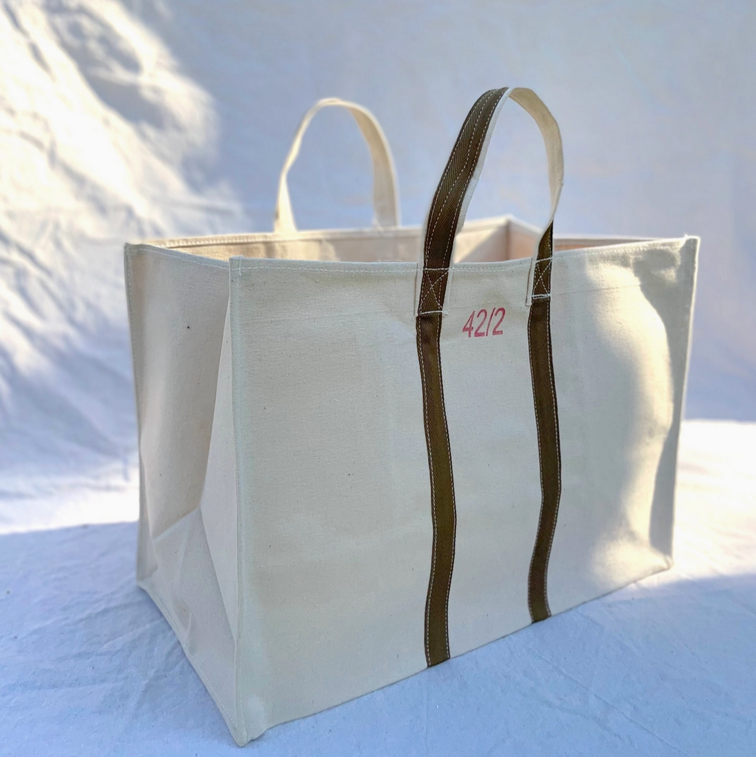Large white tote bag with brown handles on a light blue background - Little-ish