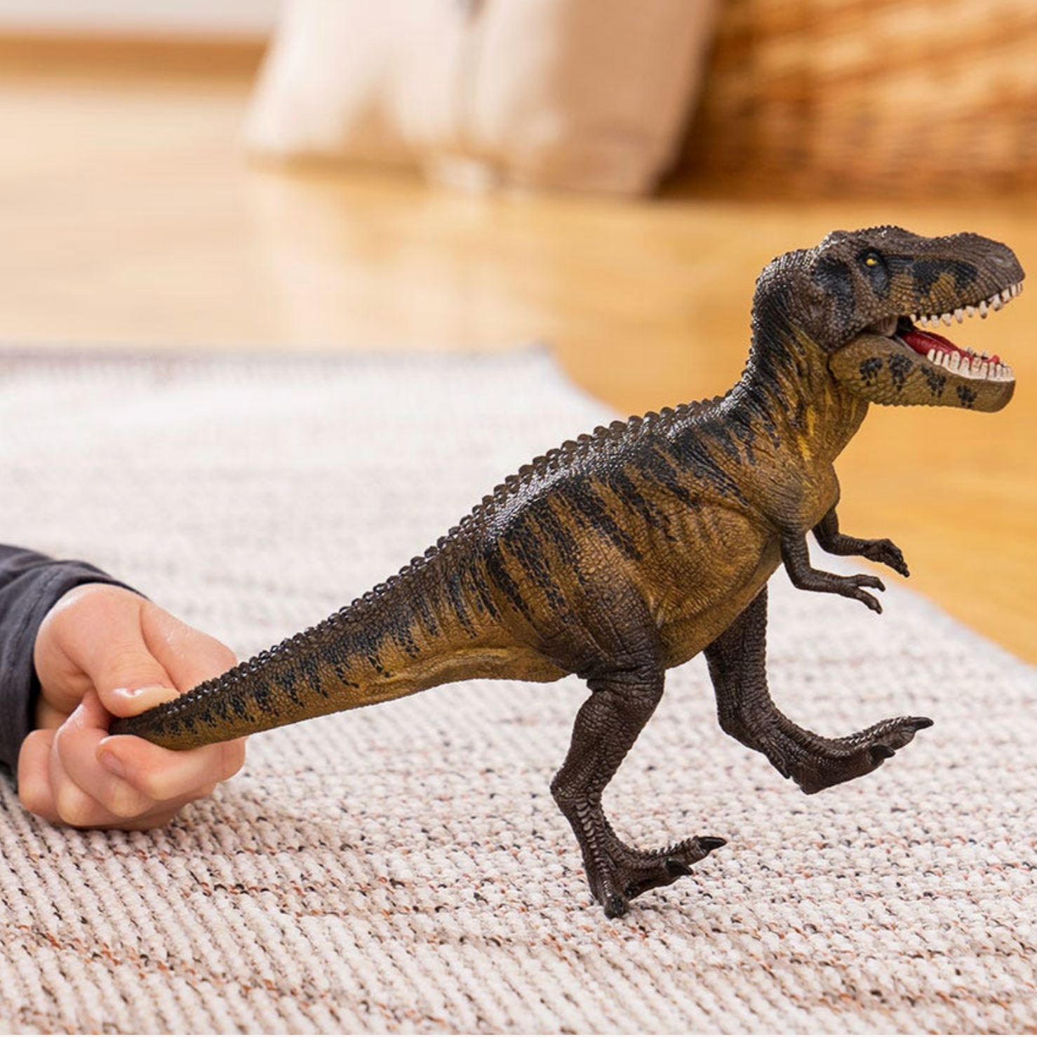 Toy dinosaur being held by a person on a textured surface - Little-ish