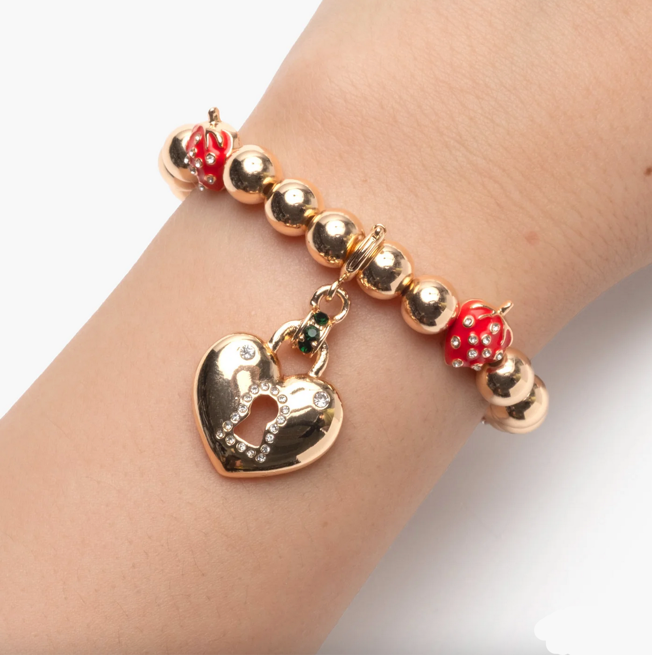 Gold bracelet with heart charm and red beads on a wrist against a white background - Little-ish