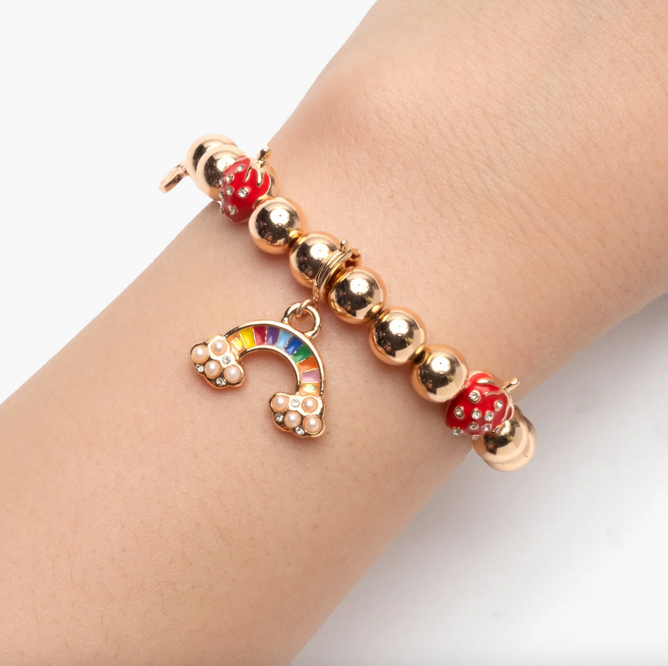 Bracelet with gold beads and a rainbow charm on a wrist against a white background - Little-ish