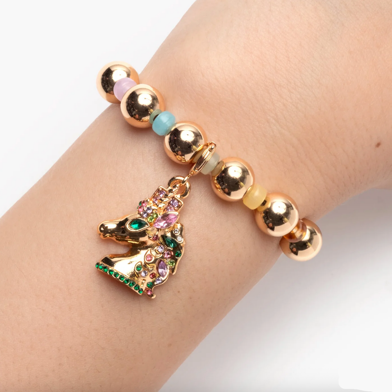 Bracelet with gold beads and a colorful unicorn charm on a wrist. - Little-ish