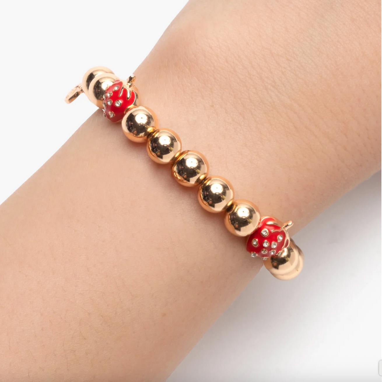 Gold bracelet with red dice-shaped charms on a wrist against a white background - Little-ish