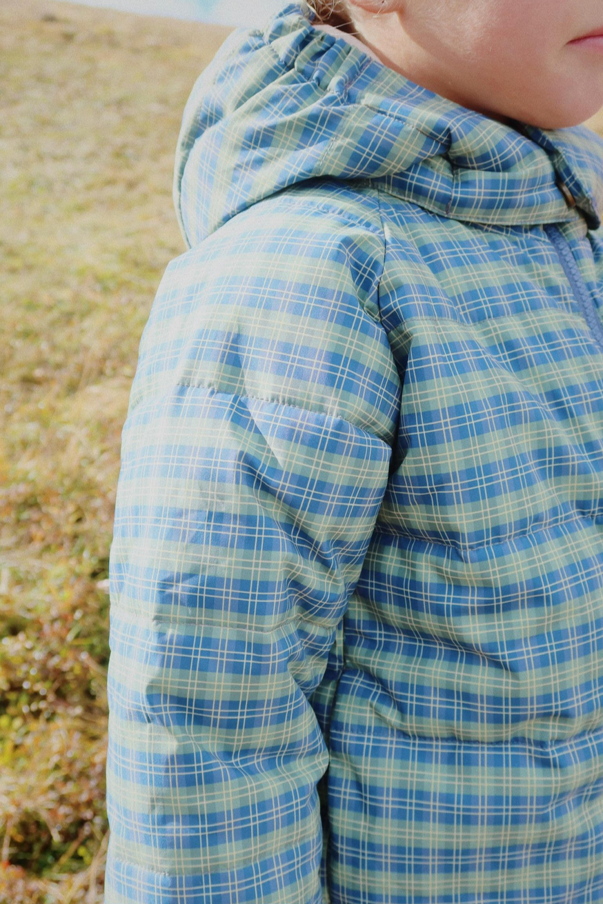 Person wearing a blue and green plaid jacket with a blurred natural background - Little-ish
