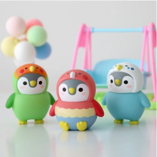 Three colorful penguin figurines with a baby bouncer and balloons in the background