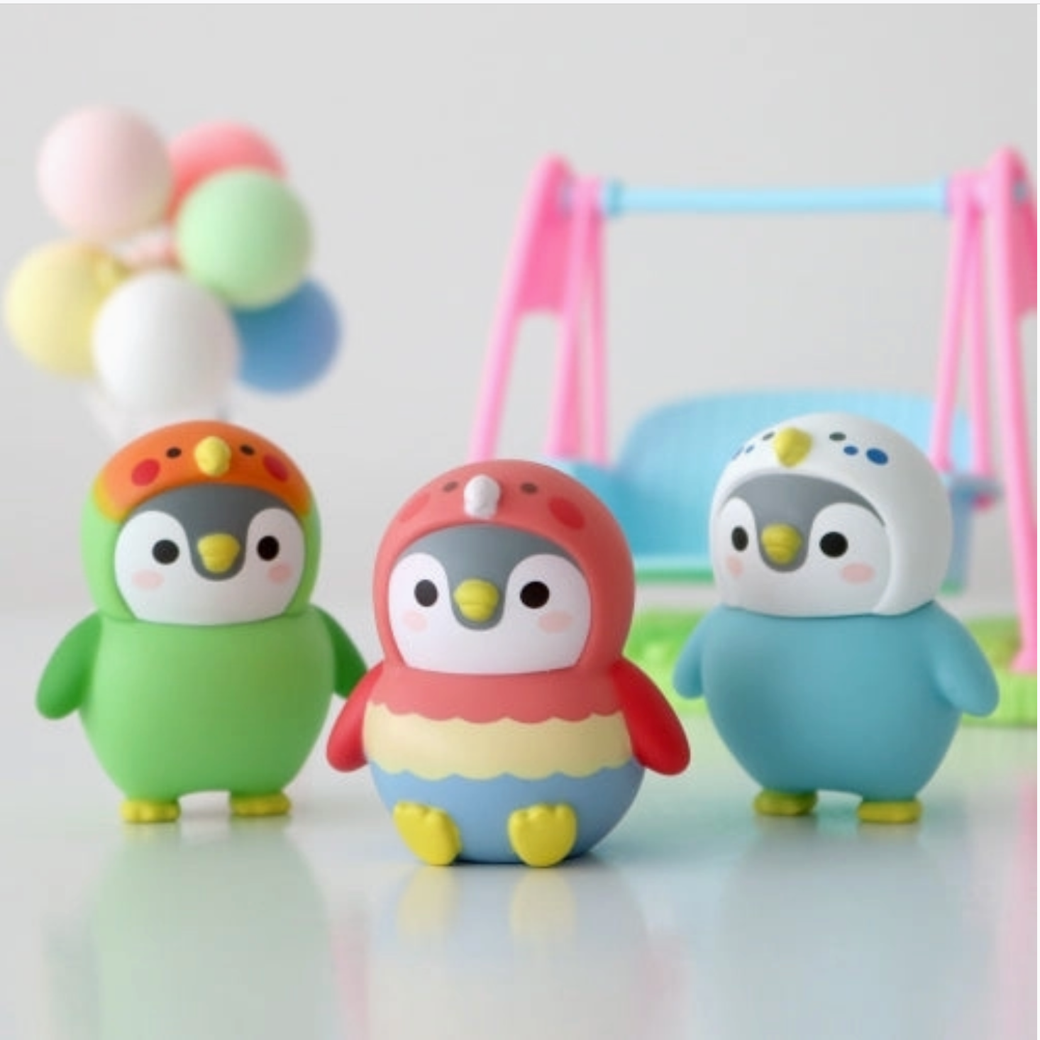 Three colorful penguin figurines with a baby bouncer and balloons in the background - Little-ish