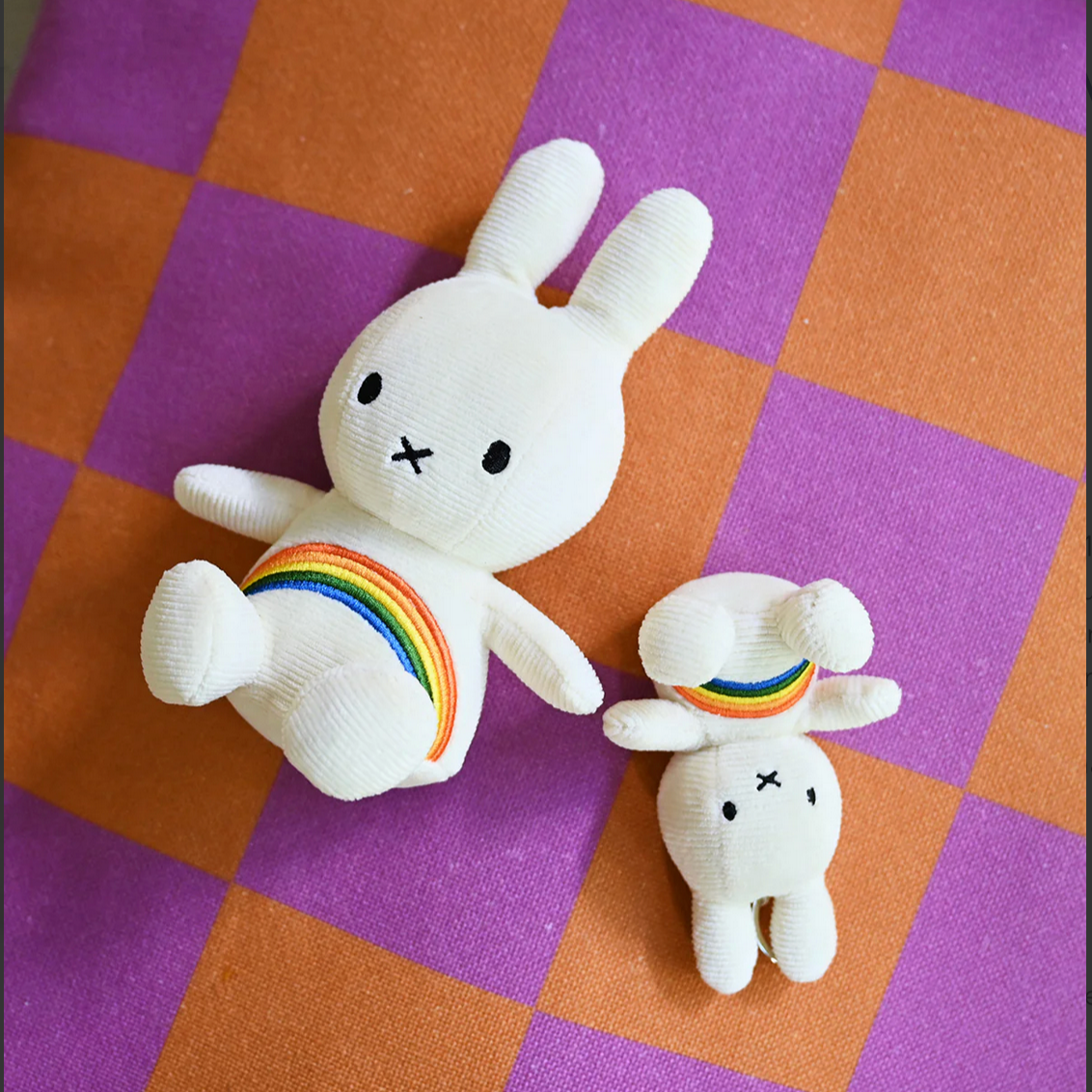 Two white plush toys with rainbow patterns on a checkered purple and orange surface