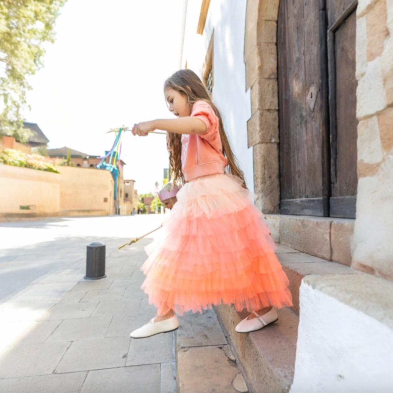 Young girl in a pink dress standing on a stone path with a building in the background - Little-ish
