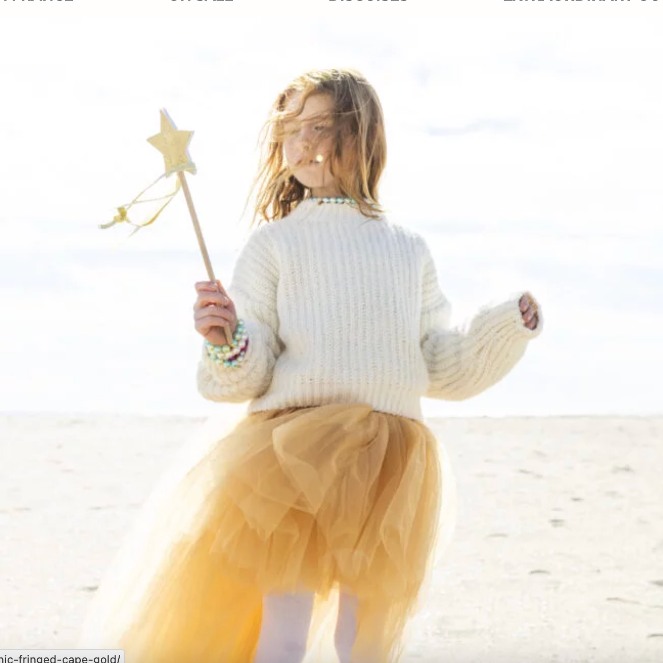 Child in a white sweater and yellow skirt holding a star-shaped wand on a beach. - Little-ish