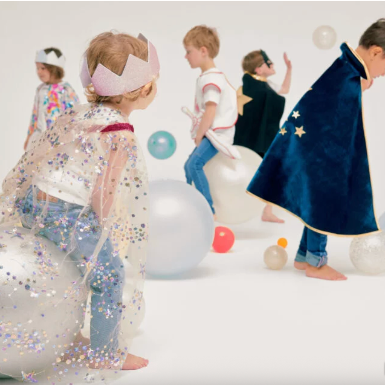 Children in costumes playing on a white floor with colorful balloons. - Little-ish