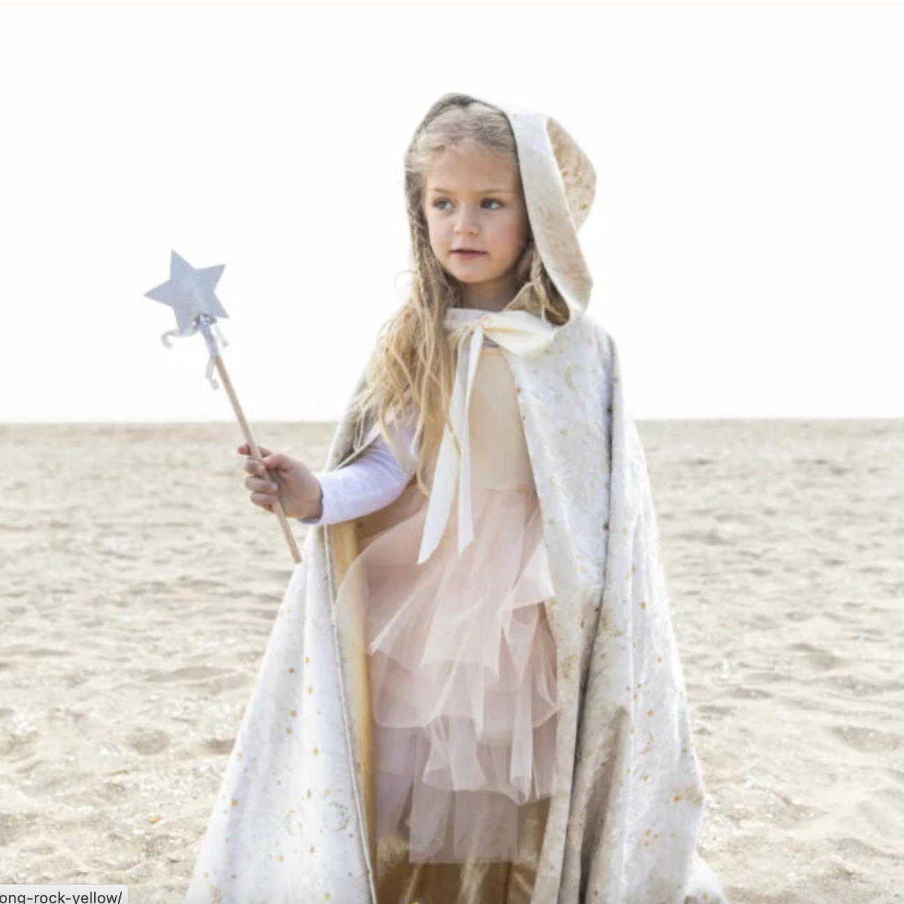 Young girl in a fairy costume holding a wand on a sandy background